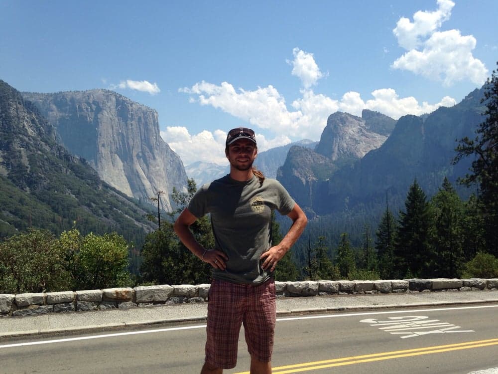 Man posing on a road overlooking the iconic granite cliffs of Yosemite Valley.